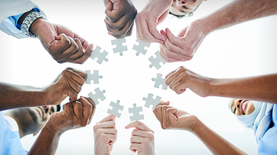 Group of people with outstretched hands holding puzzle pieces in a circle.